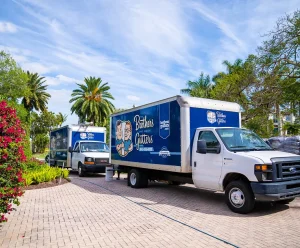 Two Brothers Gutters service trucks parked on a residential driveway surrounded by palm trees and landscaping.