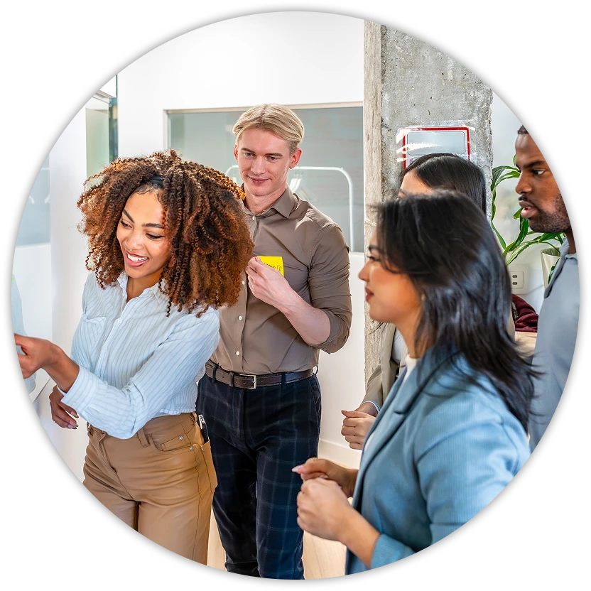 Group of coworkers standing by a glass wall covered with notes, smiling and brainstorming together in an office.